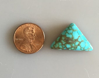 May include: A turquoise cabochon in a triangle shape, next to a US penny for size comparison. The turquoise is a vibrant blue-green color with brown matrix.