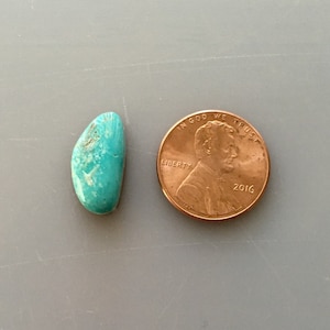 May include: A turquoise cabochon gemstone, approximately the size of a US penny. The stone is a light blue-green color with brown matrix.
