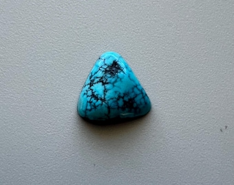 May include: A triangular turquoise gemstone with a polished surface. The stone features a vibrant blue color with intricate black veining patterns throughout. The gemstone is set against a neutral gray background.