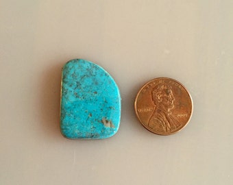 May include: A turquoise cabochon gemstone, approximately the size of a US penny.