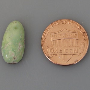 May include: A green, oval-shaped turquoise cabochon, approximately the size of a US penny.