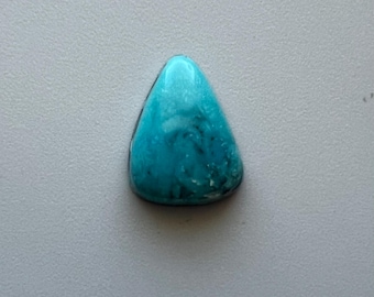 May include: A triangular, polished turquoise gemstone with a smooth, glossy surface. The stone displays a mix of light and dark blue hues with subtle veining, set against a neutral background. This gemstone is ideal for jewelry making.