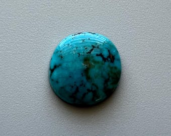 May include: A round, polished turquoise gemstone with a vibrant blue hue and dark brown matrix patterns. The stone has a smooth, glossy surface and is set against a neutral gray background. This gemstone is suitable for jewelry making.
