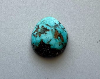 May include: A polished, oval-shaped turquoise gemstone with a vibrant blue-green hue. The stone features dark brown and black matrix patterns, creating a unique and natural design. The gemstone is set against a neutral gray background.