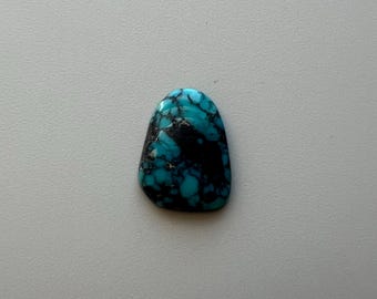 May include: A polished turquoise gemstone with a rounded top and a dark, irregular pattern. The stone's surface displays a mix of vibrant blue and black hues, creating a striking contrast. The gemstone is likely used for jewelry or decorative purposes.