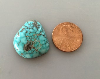 May include: A turquoise cabochon stone, approximately the size of a US penny. The stone has a blue-green color with brown and black matrix.