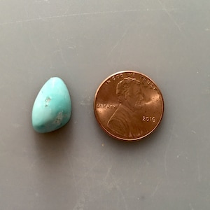 May include: A turquoise stone cabochon, approximately the size of a US penny. The stone is a light blue color with brown markings.  "In God We Trust" and "Liberty" are visible on the penny.