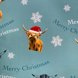 Op de afbeelding: Blauw en wit kerstpapier met een herhalend patroon van Schotse Hooglanders met kerstmanmutsen, sneeuwvlokken en de tekst "Merry Christmas".