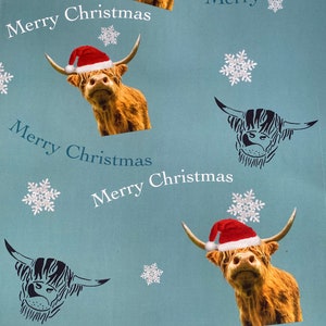 Op de afbeelding: Blauw inpakpapier met een herhalend patroon van Schotse Hooglanders met kerstmanmutsen en sneeuwvlokken. De tekst "Merry Christmas" wordt herhaald in het hele patroon.