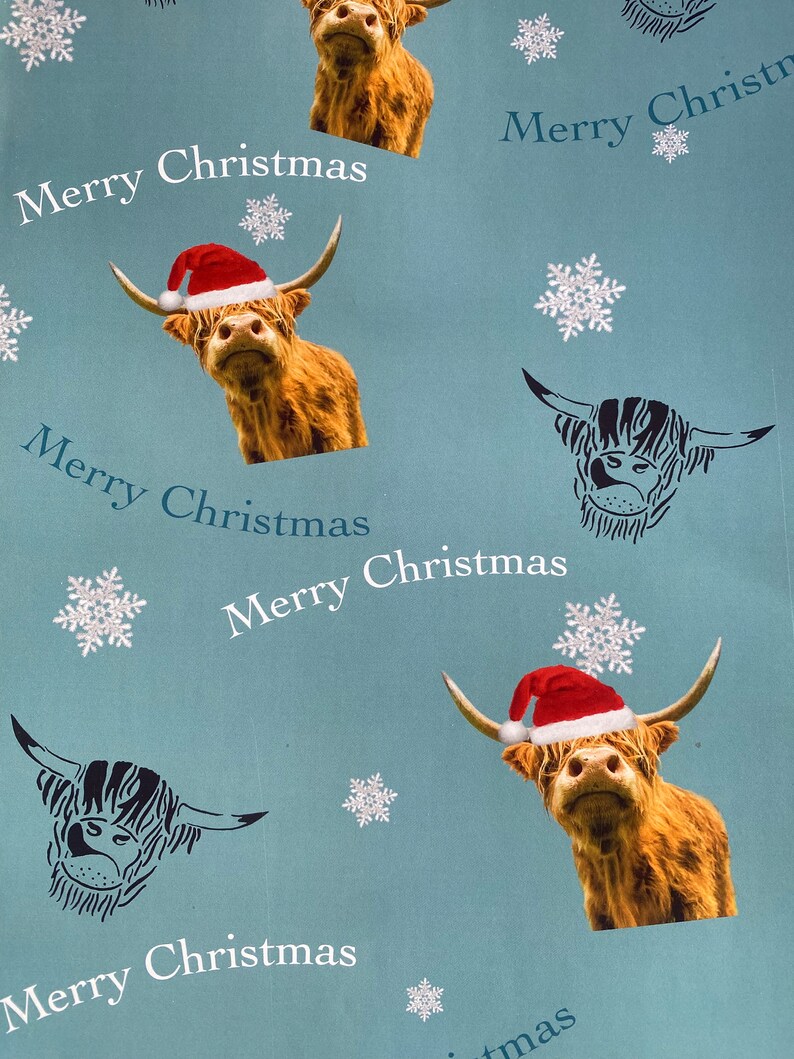 Op de afbeelding: Blauw inpakpapier met een herhalend patroon van Schotse Hooglanders met kerstmanmutsen en sneeuwvlokken. De tekst "Merry Christmas" wordt herhaald in het hele patroon.