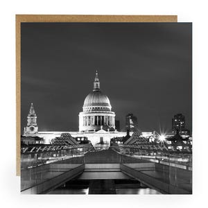 May include: Black and white photograph of St. Paul's Cathedral in London at night. The iconic dome is illuminated, with a bridge in the foreground. The image is set against a dark sky.