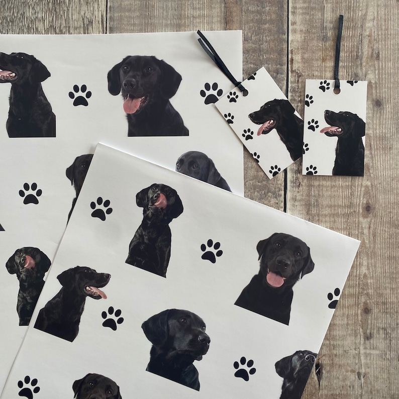 May include: Black and white wrapping paper with a paw print and black labrador retriever dog design. The paper is printed with the words "Happy Birthday".