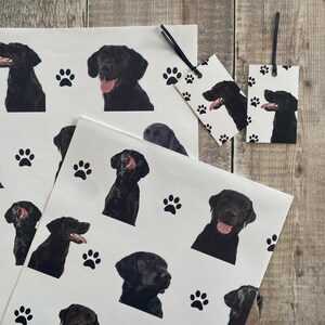 May include: Black and white wrapping paper with a paw print and black labrador retriever dog illustrations. The paper is designed for gift wrapping.