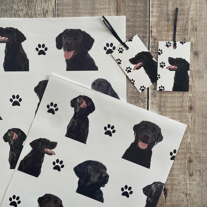 May include: Black and white wrapping paper with a paw print and black labrador retriever dog illustrations. The paper is designed for gift wrapping.