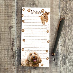 May include: A rectangular notepad with a dog theme. The notepad has a white background with brown paw prints and the word "Notes". A black pen with a gold accent is also present.