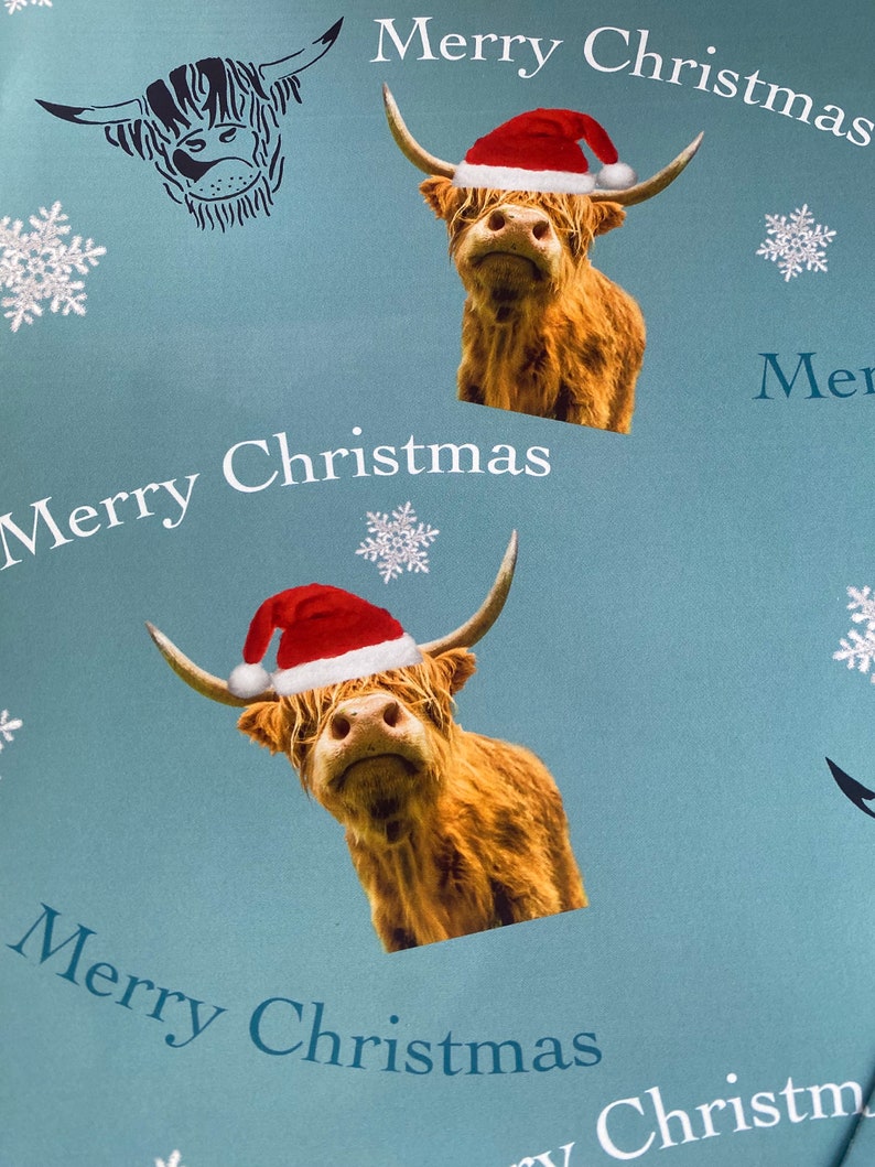 Op de afbeelding: Een blauwe achtergrond met een herhalend patroon van Schotse Hooglanders die kerstmanmutsen dragen en de tekst "Merry Christmas".
