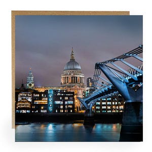 May include: A nighttime cityscape of London featuring St. Paul's Cathedral and the Millennium Bridge. The image is set against a dark, cloudy sky, with the city lights reflecting on the water below. The card has a brown border.