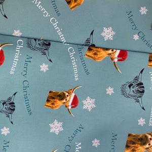 Op de afbeelding: Blauw inpakpapier met een herhalend patroon van Schotse Hooglanders met kerstmanmutsen en sneeuwvlokken. De tekst "Merry Christmas" wordt herhaald in het hele patroon.