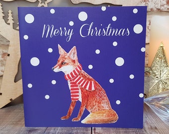 May include: A purple Christmas card with a red fox wearing a red and white scarf. The card has white snowflakes and the text "Merry Christmas" on it.