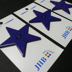 May include: Three dark blue star-shaped buttons, each attached to an individual white rectangular display card. Each card features the blue text JHB and a small logo with four colored dots. The buttons have two holes in the center for sewing.
