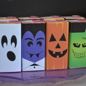 May include: Six Halloween-themed juice boxes with different characters: a ghost, a vampire, a pumpkin, and a Frankenstein. The boxes are arranged in a row on a purple tray.