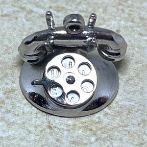 以下が含まれることがあります： ダイヤル式の電話の銀製の置物で、詳細なダイヤルとクラシックなデザインが特徴です。