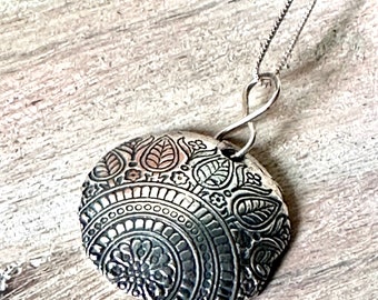 May include: A silver necklace with a round pendant featuring an intricate black and white floral design.