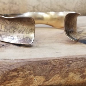 May include: A gold-toned metal cuff bracelet with a textured, wavy design. The bracelet has a hammered finish and a slightly curved shape.