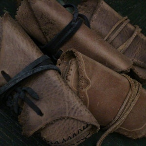 May include: Four brown leather pouches with stitching and tied with leather straps. The pouches are arranged in a pile on a green surface.