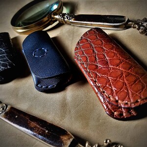 May include: Three leather keychains with different patterns and colors. One is black with a textured pattern, one is blue with a stitched design, and one is brown with a crocodile pattern.