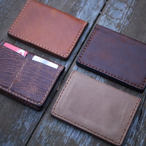 May include: Four leather wallets in different colors and styles. The wallets are laid out on a wooden surface.