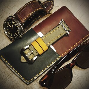 May include: A leather watch strap with a black face watch, a leather watch band with a yellow and gray strap, and a pair of brown sunglasses.