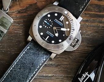 May include: A black and silver Panerai Submersible watch with a blue second hand and a black leather strap. The watch face has white markings and the text "PANERAI SUBMERSIBLE" and "AUTOMATIC 300m/1000ft".