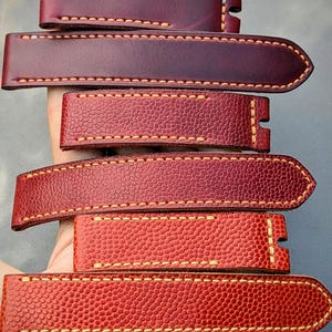 May include: Five different leather watch straps in various shades of red with contrasting yellow stitching. The straps are made of a textured leather with a pebbled surface.