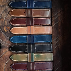 May include: A set of eight leather watch straps in various colours, including brown, tan, blue, black, and green. Each strap has contrasting stitching and a double keeper.