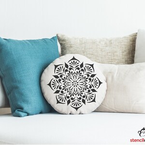 May include: A white throw pillow with a black mandala design. The pillow is sitting on a white couch with other pillows.