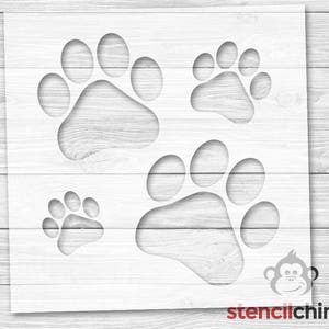 May include: A stencil sheet with four paw print designs. The stencil sheet is white and has a wood grain background.