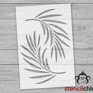 May include: A white stencil with a design of two overlapping branches of leaves. The stencil is on a wood background.