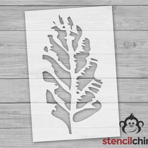 May include: A white stencil of a leafy branch with a detailed design. The stencil is on a wood background.