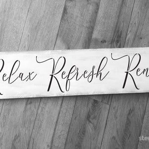 May include: White wooden sign with black calligraphy that reads "Relax Refresh Renew".
