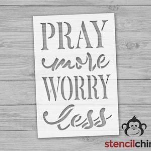 Op de afbeelding: Witte stencil met de woorden "Pray more Worry less" in een decoratief lettertype. De stencil is op een houten achtergrond.