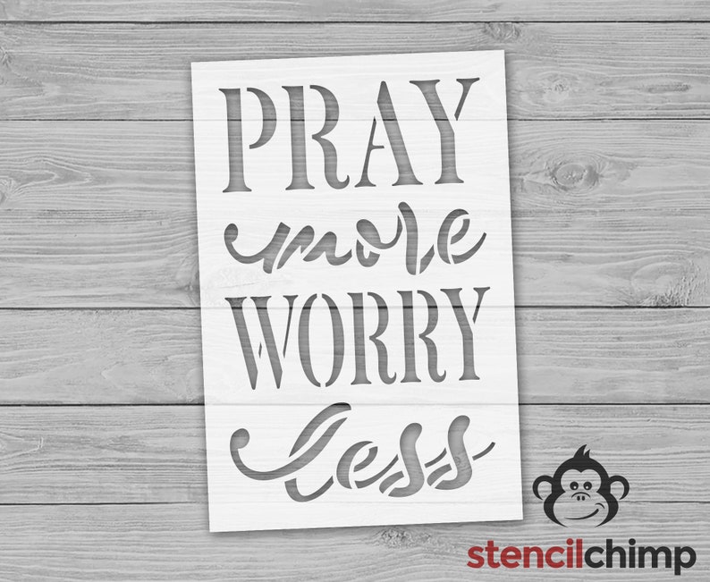 Op de afbeelding: Witte stencil met de woorden "Pray more Worry less" in een decoratief lettertype. De stencil is op een houten achtergrond.