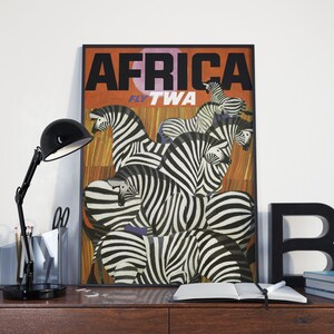 Op de afbeelding: Een vintage reisposter die vluchten naar Afrika met TWA adverteert. De poster toont een groep zebra's met zwart-witte strepen tegen een achtergrond van oranje en bruine strepen. De tekst "AFRICA" staat in grote zwarte letters bovenaan de poster, en "FLY TWA" staat in kleinere zwarte letters eronder.