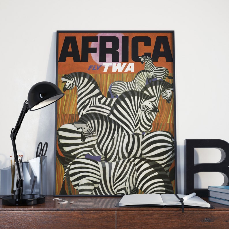 Op de afbeelding: Een vintage reisposter die vluchten naar Afrika met TWA adverteert. De poster toont een groep zebra's met zwart-witte strepen tegen een achtergrond van oranje en bruine strepen. De tekst "AFRICA" staat in grote zwarte letters bovenaan de poster, en "FLY TWA" staat in kleinere zwarte letters eronder.