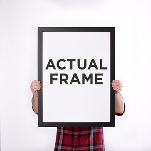 May include: A black rectangular frame with the words "ACTUAL FRAME" in bold, black letters on a white background. The frame is held up by a person wearing a red and black plaid shirt.