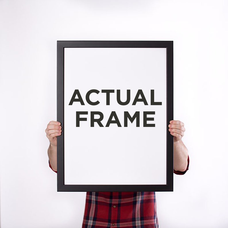 May include: A black rectangular frame with the words "ACTUAL FRAME" in bold, black letters on a white background. The frame is held up by a person wearing a red and black plaid shirt.