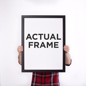 May include: A black rectangular frame with the words "ACTUAL FRAME" in bold, black letters on a white background. The frame is held up by a person wearing a red and black plaid shirt.