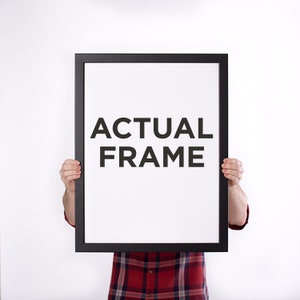 May include: A person is holding a black picture frame in front of their body. The frame has the words "ACTUAL FRAME" printed in black text on a white background.