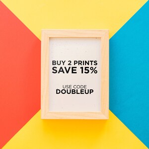May include: A light wooden picture frame with the text "BUY 2 PRINTS SAVE 15% USE CODE DOUBLEUP" on a white background. The frame is set against a background of red, yellow, and blue geometric shapes.