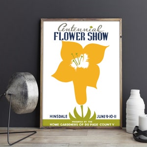 May include: A framed poster for the Centennial Flower Show. The poster features a large yellow flower illustration against a white background. Text includes "Centennial Flower Show," "Hinsdale," and the date "June 9-10-11."